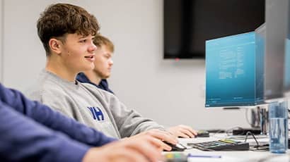 Three young male adults sit in front of computer screens in a seminar room. 