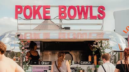 The front of a silver food truck selling poke bowls at a festival wiht people queueing in front of it. 