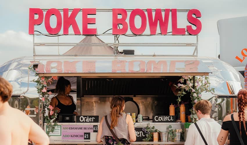 The front of a silver food truck selling poke bowls at a festival wiht people queueing in front of it. 