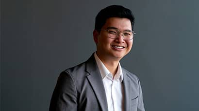 A head and shoulders shot of a man wearing a grey suit against a grey background