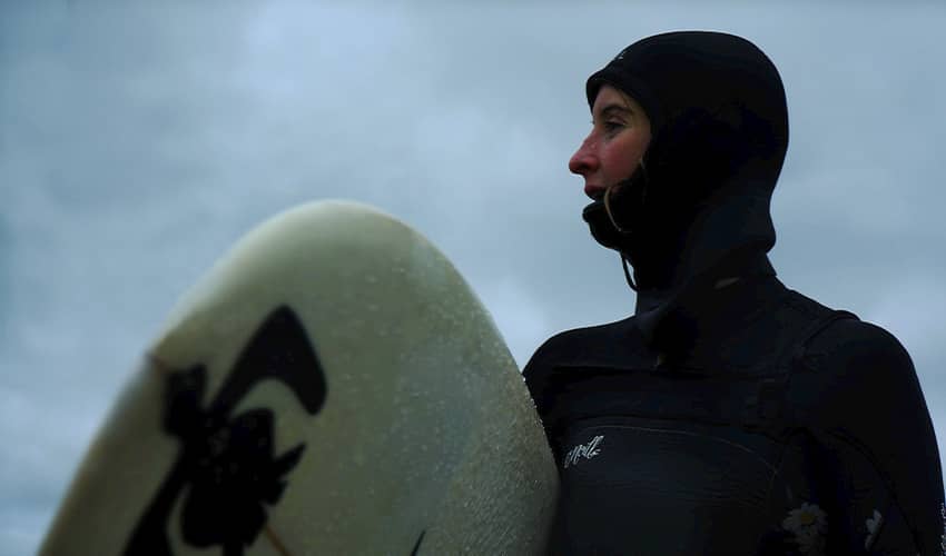 A head and shoulders shot of a person wearing a wet suit and holding a surfboard.