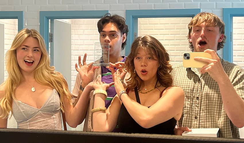 Four students take a selfie in a mirror while holding an award.
