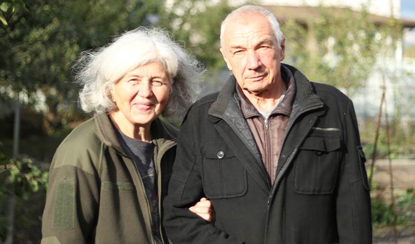 A couple stand in a garden arm in arm