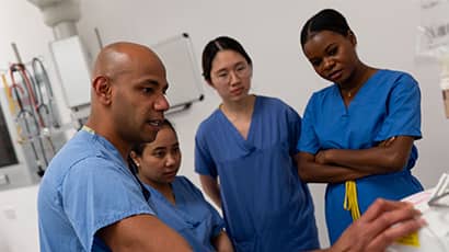 Four people wearing hospital scrubs in a healthcare setting gather around a piece of hospital equipment.