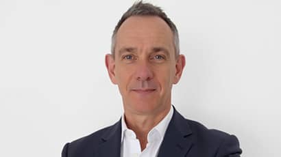 A man wearing a dark suit and white shirt looks at the camera. 