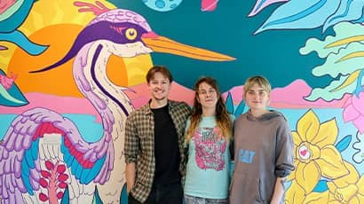 Three people stand in front of a painted colourful wildlife mural