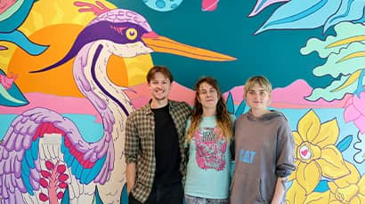 Three people stand in front of a painted colourful wildlife mural