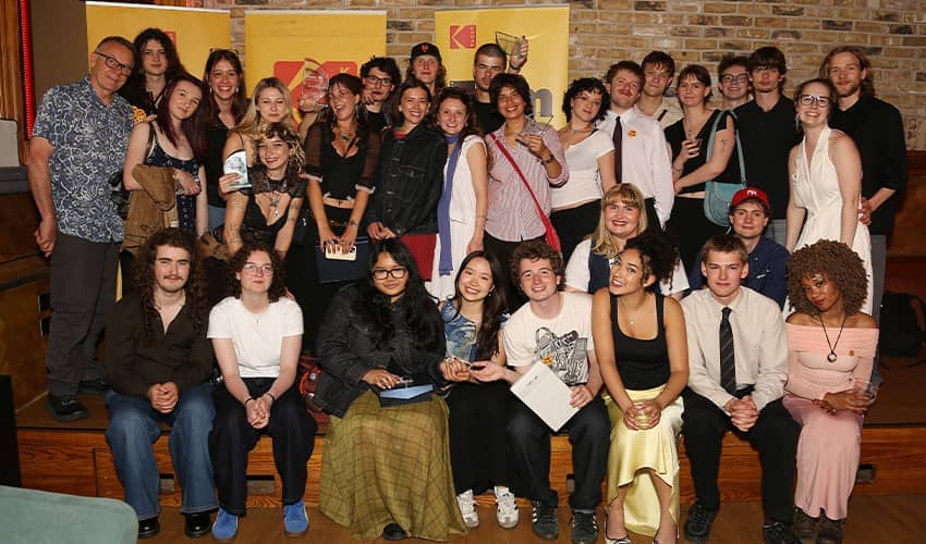 Group photo of about 30 people pose together indoors at an awards event, with several holding certificates and smiling toward the camera.
