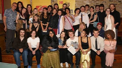 Group photo of about 30 people pose together indoors at an awards event, with several holding certificates and smiling toward the camera. 