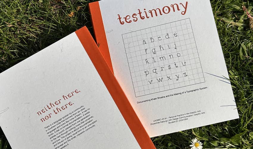 Two orange-and-white booklets displayed on grass, featuring a typographic design. 