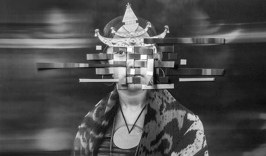 Black-and-white portrait of a person wearing an ornate headpiece, against a blurred background.
