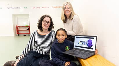 Two women and a child sit in a school setting with a laptop