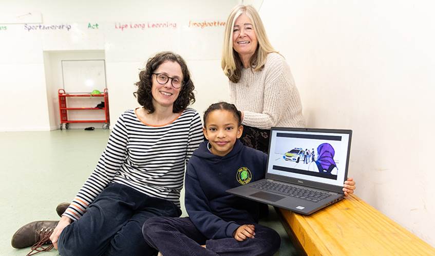 Two women and a child sit in a school setting with a laptop
