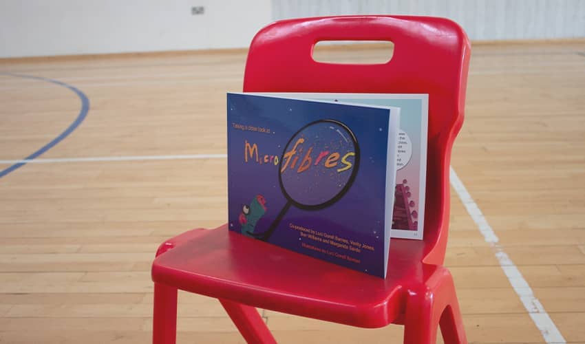 A blue book named 'Microfibres' propped on a red chair in a sports hall. 