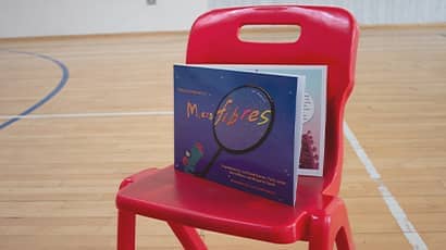 A blue book resting on a red chair in a sports hall