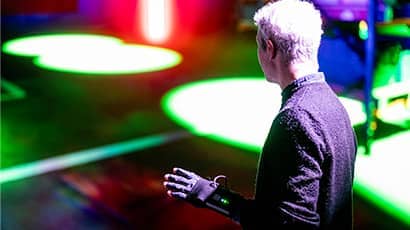 The back of a man wearing a technologically advanced pair of gloves, with brightly coloured digital shapes in the background