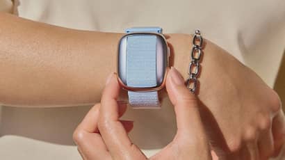 A close up of a blue watch on a wrist. The watch doesn't have a face but has the same shape as a smartwatch. 