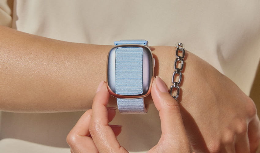 A close up of a blue watch on a wrist. The watch doesn't have a face but has the same shape as a smartwatch. 