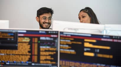 Two people working on computers displaying trading information.