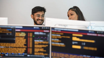 Two people working on computers displaying trading information.