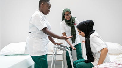 Two women in occupational therapy helping a patient to get up from a bed.