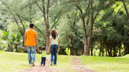 Parents walking with their child on a woodland path.