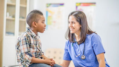 Nurse speaking with a young black boy as he sits on a table.