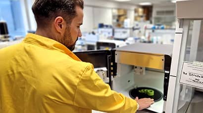 A male researcher in a yellow lab coat reaching in to a 3D food printer to retrieve some 3D printed food