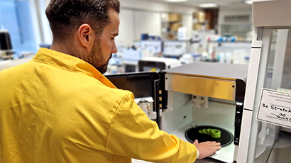 A male researcher in a yellow lab coat reaching in to a 3D food printer to retrieve some 3D printed food