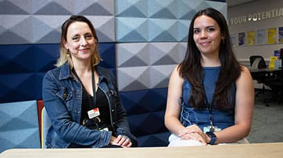Two women seated and smiling at the camera, with a patterned blue background