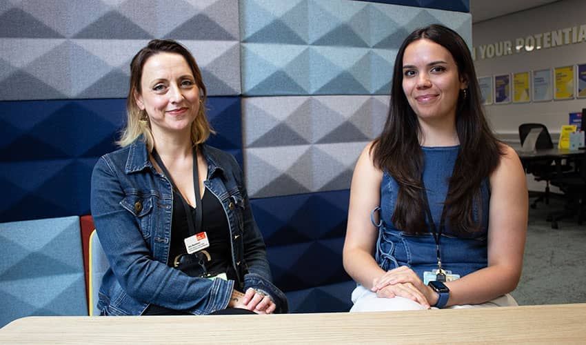 Two women seated and smiling at the camera, with a patterned blue background
