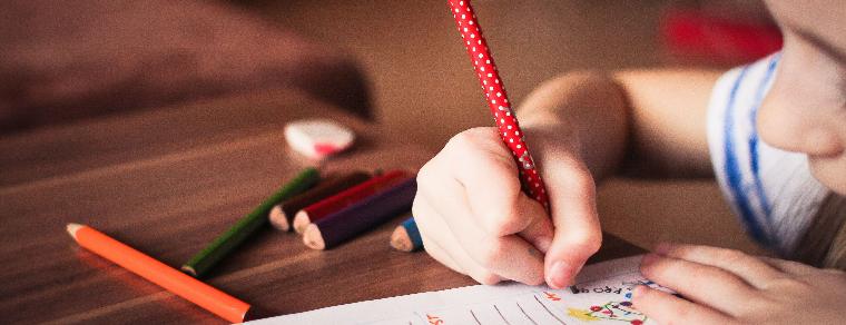 Close-up of young child writing with a pencil at a desk.