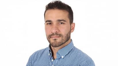 A man wearing a blue shirt looking towards the camera, with a white background