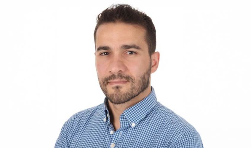 A man wearing a blue shirt looking towards the camera, with a white background