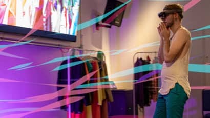 Man wearing VR headset near screen showing fashion items.