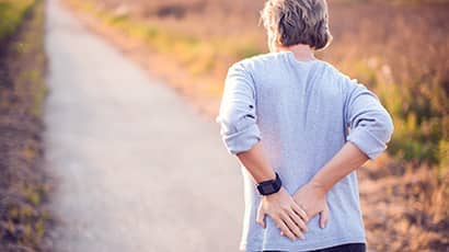Image showing a woman holding her lower back with both hands, with a path in the background