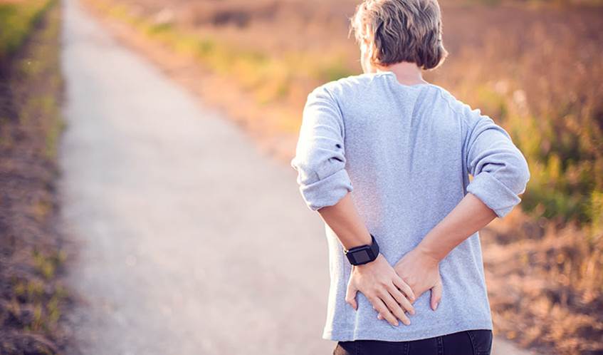 Image showing a woman holding her lower back with both hands, with a path in the background