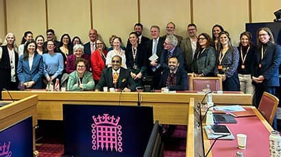 A large group of people smiling at the camera in a room, with a pink crest displayed in the foreground