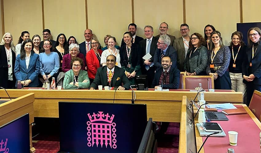 A large group of people smiling at the camera in a room, with a pink crest displayed in the foreground