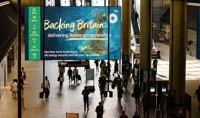 A blue and green digital advertising screen at a tube station in London