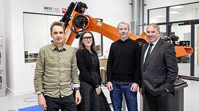 Four people stood in front of a giant orange robotic arm