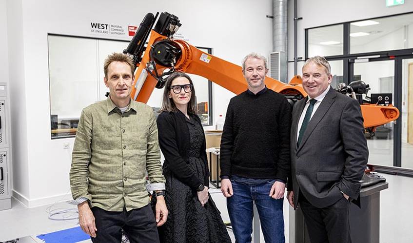Four people posing in front of a giant orange robotic arm