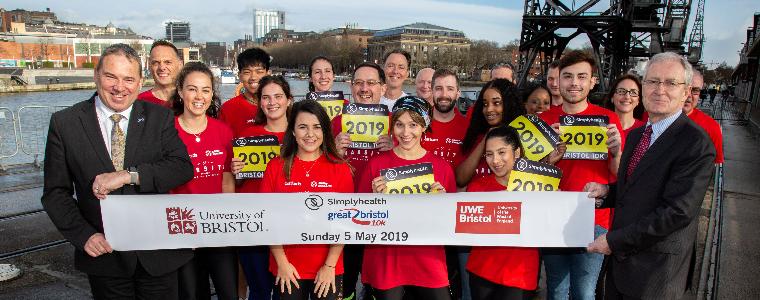 Group of runners in red t-shirts holding banner on Bristol's harbourside with Professor Steve West and Professor Hugh Brady.