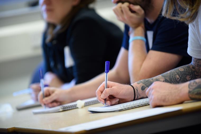 Three people sat at a desk with paper and pens.