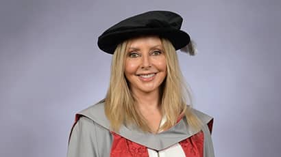 A woman smiling at the camera wearing a black graduation cap and a grey, red and white graduation gown