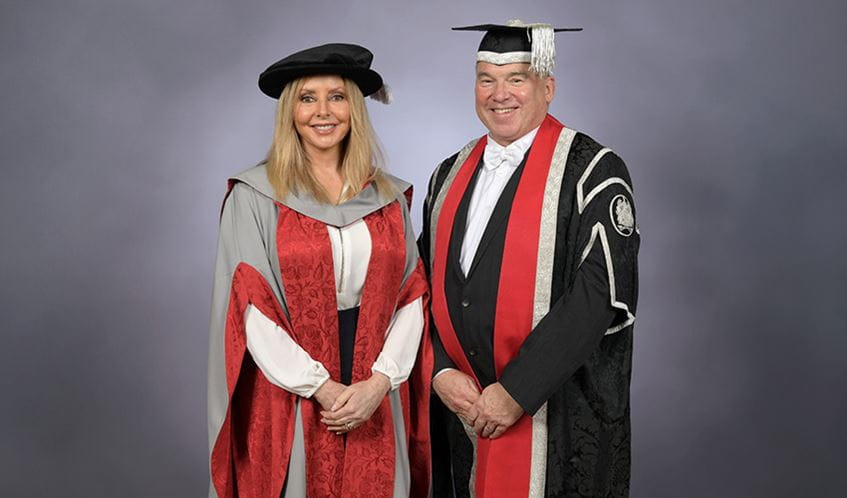 A woman and a man smiling at the camera, wearing graduation caps and gowns