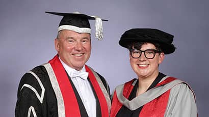 Professor Sir Steve West (left) with Clare Reddington (right), wearing black caps and red gowns at a graduation ceremony