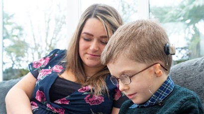 A child wearing a cochlear implant sitting with a woman.