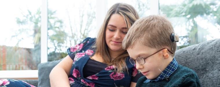 A child wearing a cochlear implant sitting with a woman.