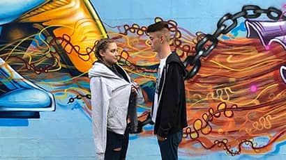 A man and a woman stand in front of some street art.